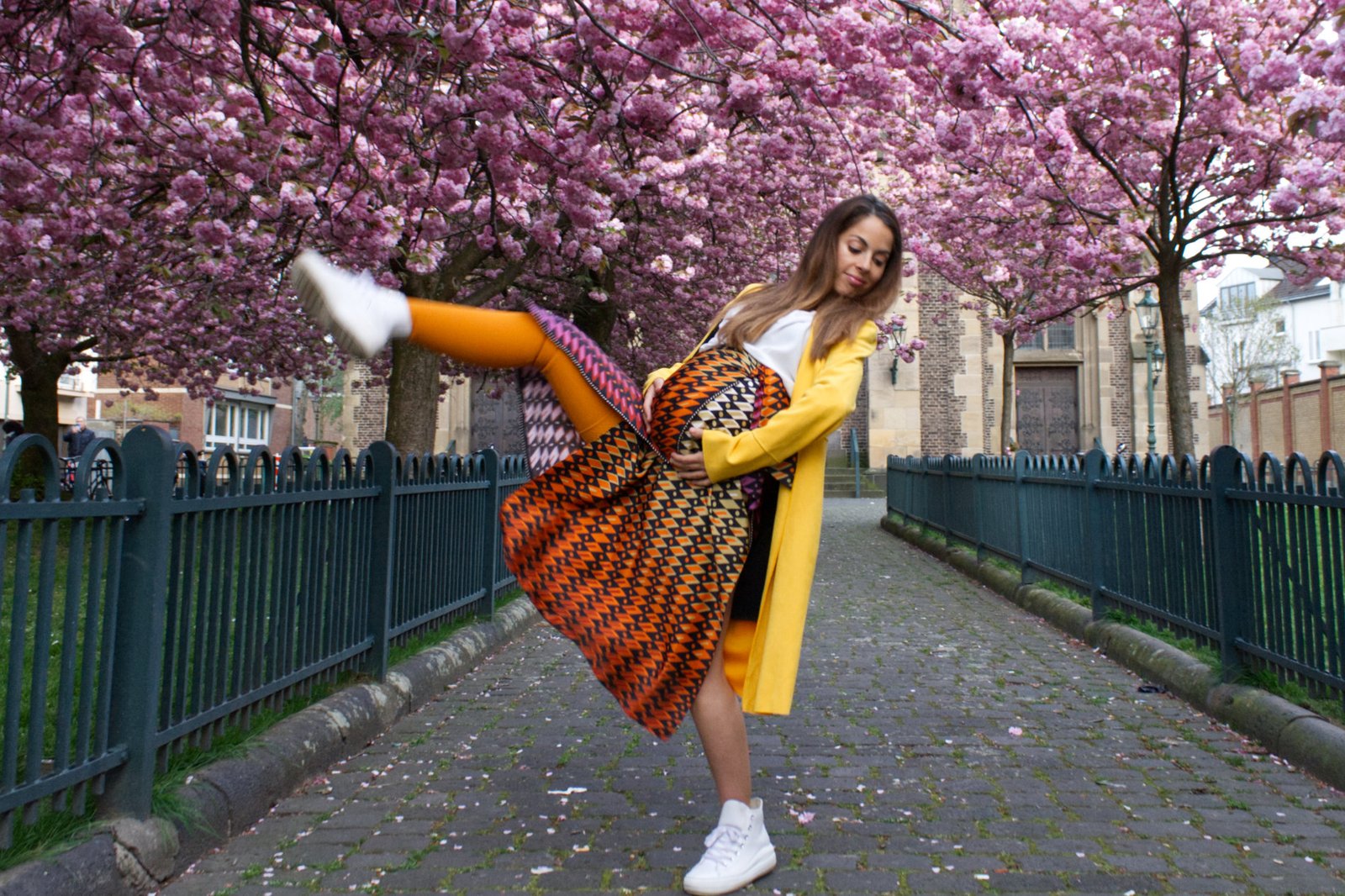 Carmen Mar with colorful dress and pregnant body dancing pose in front of cherry blossom trees