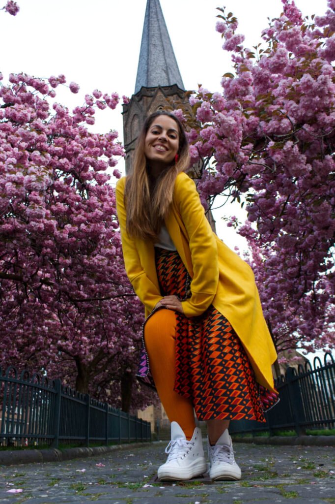 Colorful Pregnant Carmen Mar dancing pose in front of blooming cherry blossom trees and church  